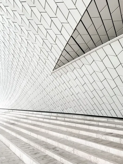 White tiled architectural wall and sweeping striped steps in a geometric interior.