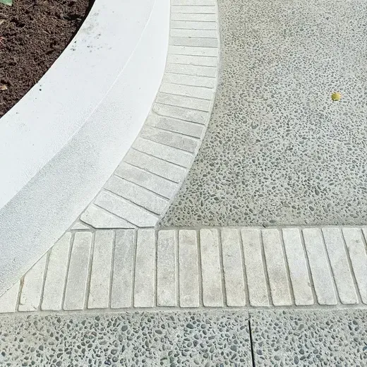 Curved white brick edging beside a light gray textured walkway and planter bed