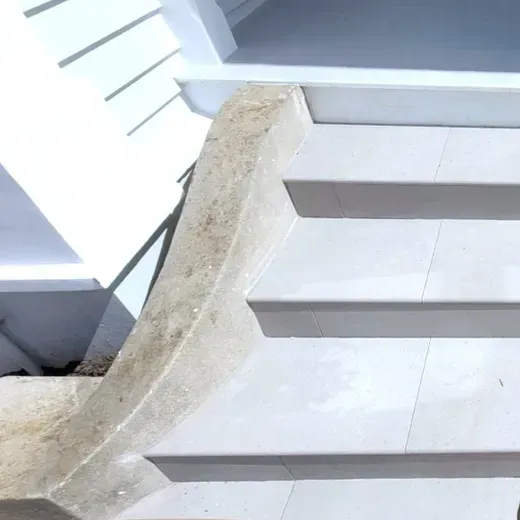 Staircase with a cracked, crumbling concrete edge beside white steps and a metal handrail