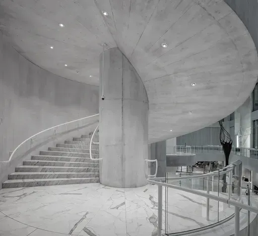 Curved marble staircase in a modern white interior with concrete columns and railings