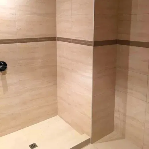 Empty tiled shower with beige walls and a square floor drain