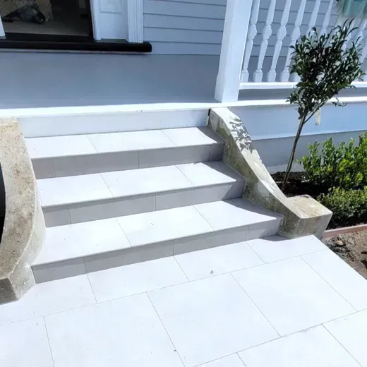 Front porch steps with white tile, flanked by stone side walls and a small shrub on the right.