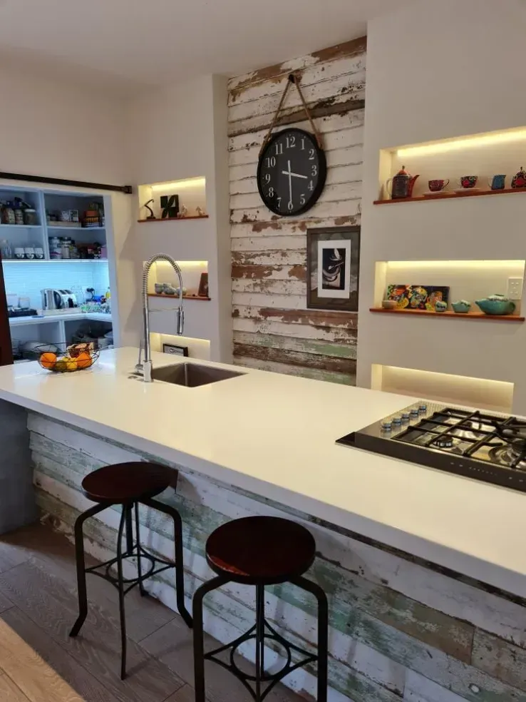 Modern kitchen bar with white countertop, rustic wood island, open shelves, and warm under-shelf lighting