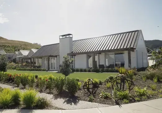 Modern house with gray metal roof, landscaped front garden, and sidewalk under a clear sky
