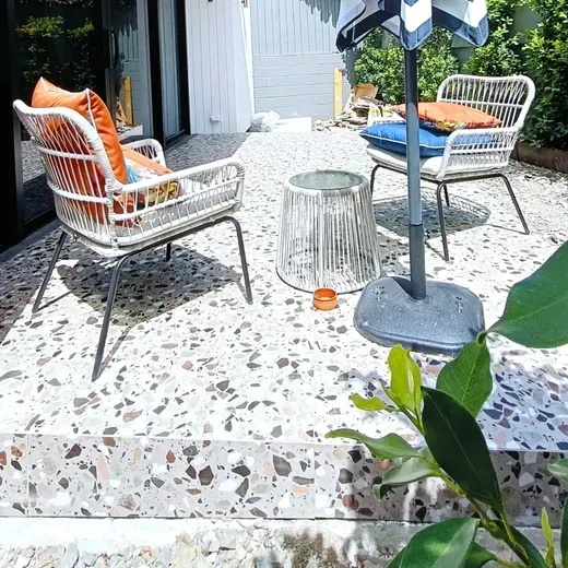 Patio seating with wicker chairs, colorful cushions, and a small glass table on a terrazzo patio.