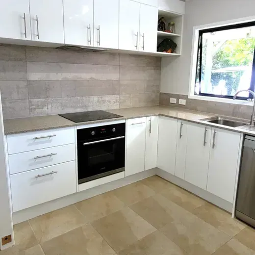 Bright modern kitchen with white cabinets, black oven, and gray tiled backsplash