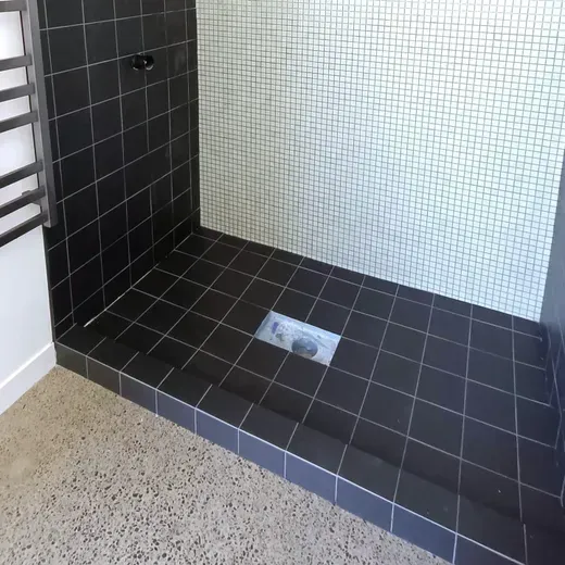 Tiled shower stall with black and white tiles and a floor drain.