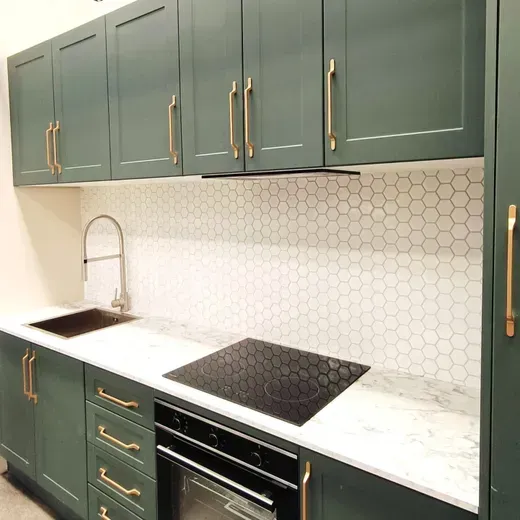 Modern kitchen with green cabinets, white countertop, hex tile backsplash, sink, and black cooktop