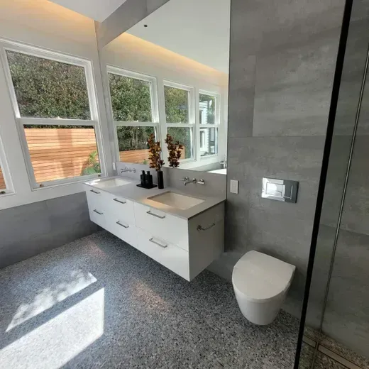 Modern bathroom with white vanity, large windows, gray tile floor, and glass shower