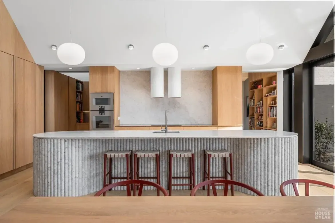Modern kitchen with curved gray-tiled island, wooden cabinets, pendant lights, and bar stools