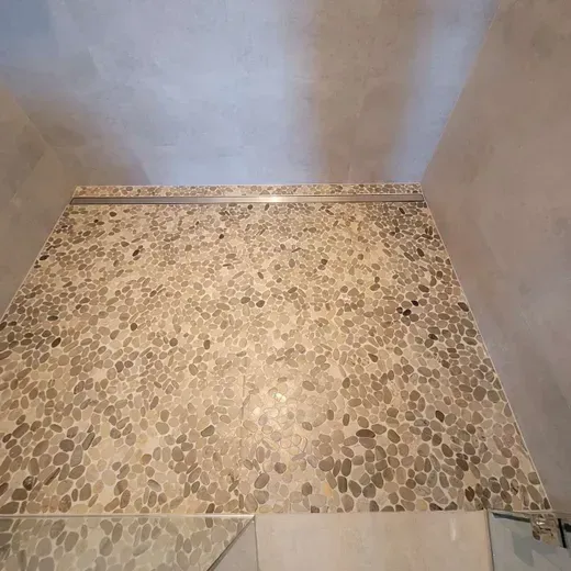 Empty stone-tiled shower floor with light gray walls and a drain