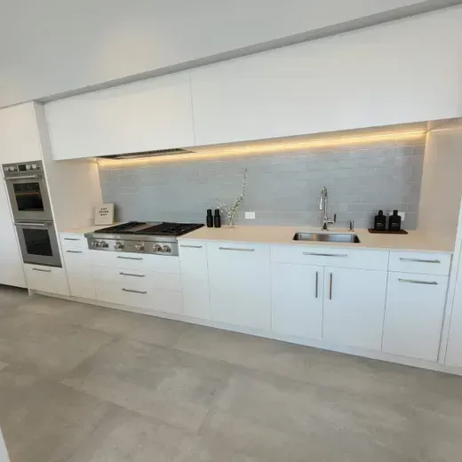 Modern white kitchen with built-in oven, cooktop, sink, and long countertop with under-cabinet lighting