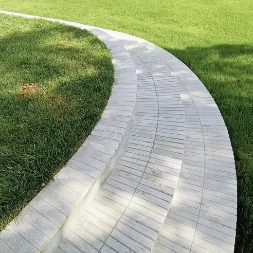 Curved light-gray paved walkway beside a green lawn in bright sunlight