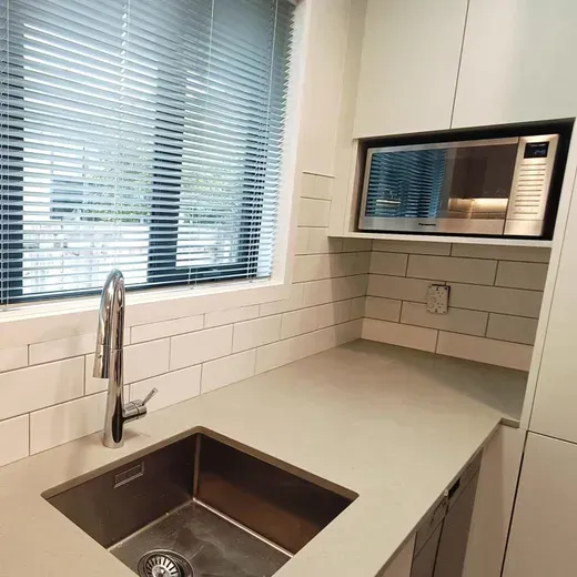 Modern kitchen with sink, large window, gray countertops, and built-in microwave