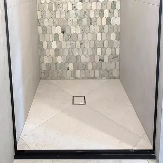 Modern walk-in shower with white tile floor, mosaic back wall, and square drain.