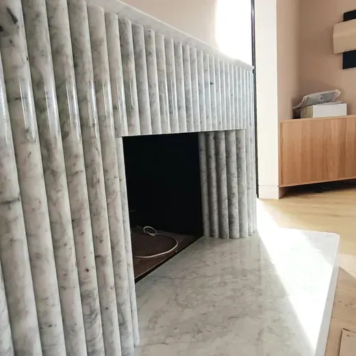 Marble fireplace with gray vertical paneling and a dark firebox in a bright modern room