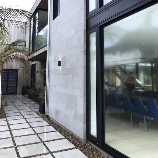 Modern building walkway with tiled path, glass windows, and a palm tree by the entrance