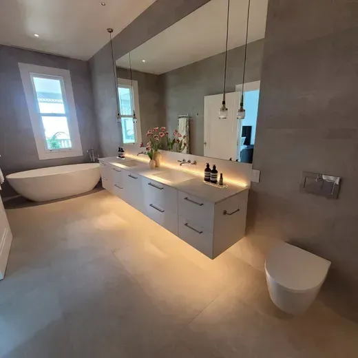 Modern gray bathroom with freestanding tub, double vanity, mirror, and toilet sinks out of view