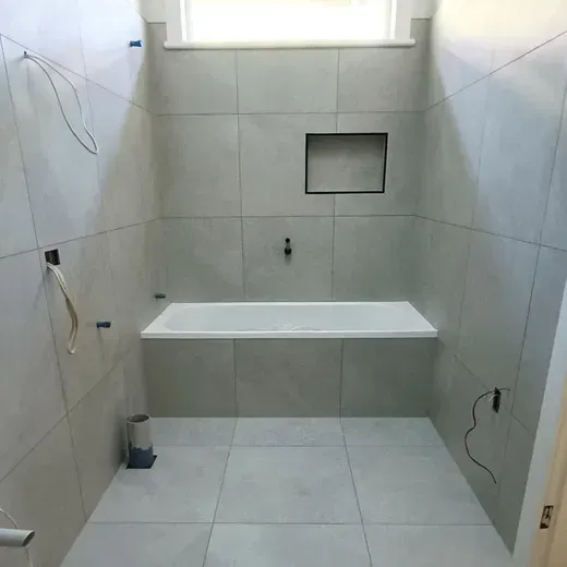 Empty tiled bathroom with a built-in bench, wall niches, and a shower area under a window