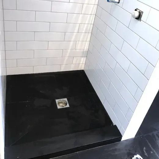 Tiled shower stall with a black shower pan and square drain in the center