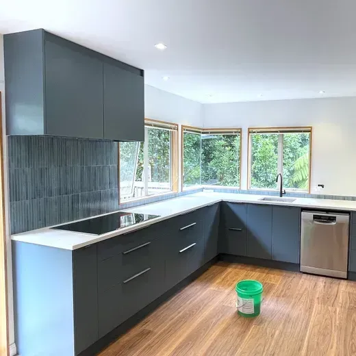 Modern kitchen with dark cabinets, white countertops, large windows, and a green bucket on the floor