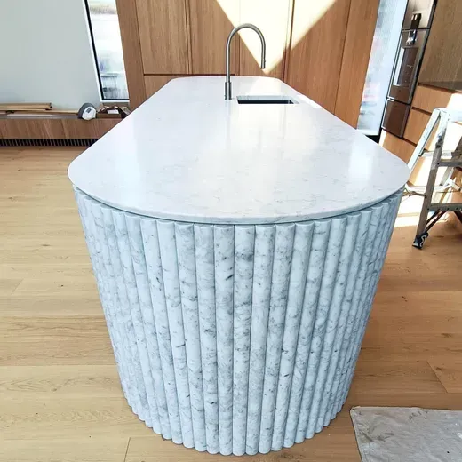 White marble-topped kitchen island with a ribbed blue-gray base and a built-in faucet in a bright room
