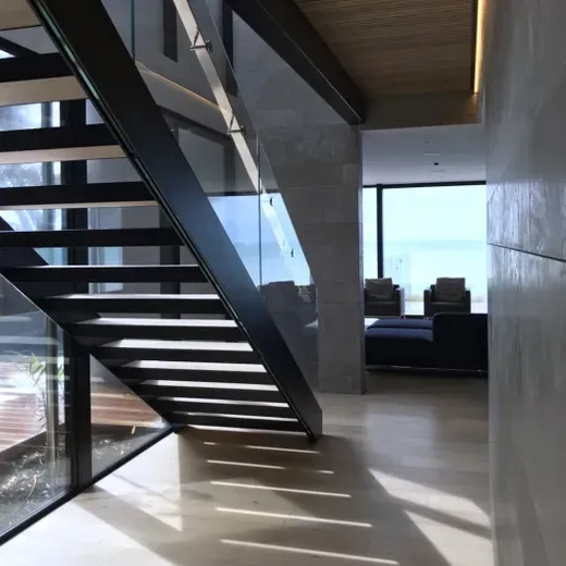 Modern interior with a black staircase, glass railing, and sunlight casting shadows across the floor