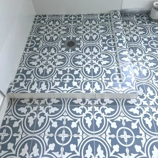 Patterned gray-and-white tiled floor with a drain near a step in a bathroom corner