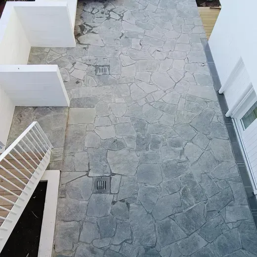 Stone-paved courtyard with white walls and a stair railing, viewed from above.