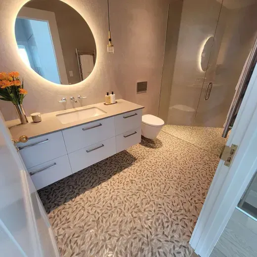 Modern bathroom with floating vanity, round mirror, pebble-pattern floor, and glass shower enclosure
