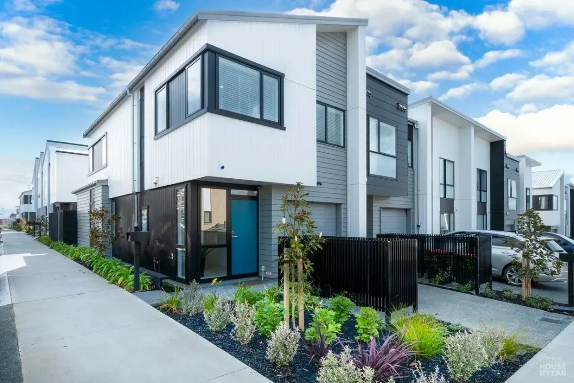 Modern two-story white townhouse row with black trim and small landscaped front gardens under a blue sky