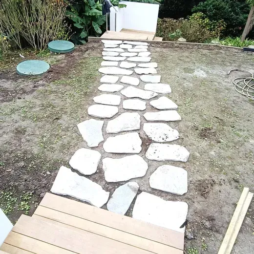 Stone stepping path through a patchy yard leading to a white gate, with green covers on the left.