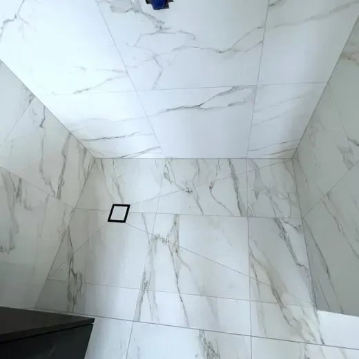 White marble-tiled room corner with a small black square fixture on the wall and a dark ledge in the foreground