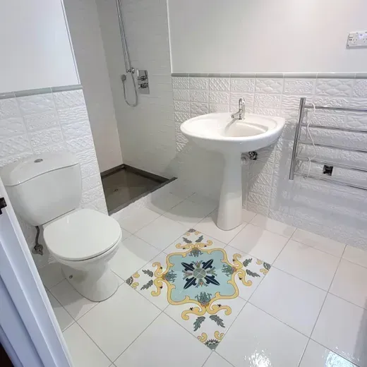Small white bathroom with toilet, pedestal sink, towel rack, and decorative floor tile.