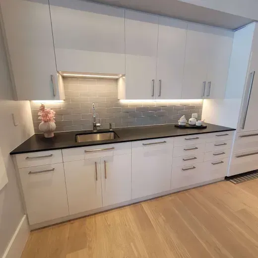 Modern white kitchen with black countertops, under-cabinet lighting, and light wood flooring