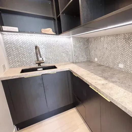 Modern kitchen corner with black cabinets, light countertops, and a stainless sink under diamond-pattern backsplash