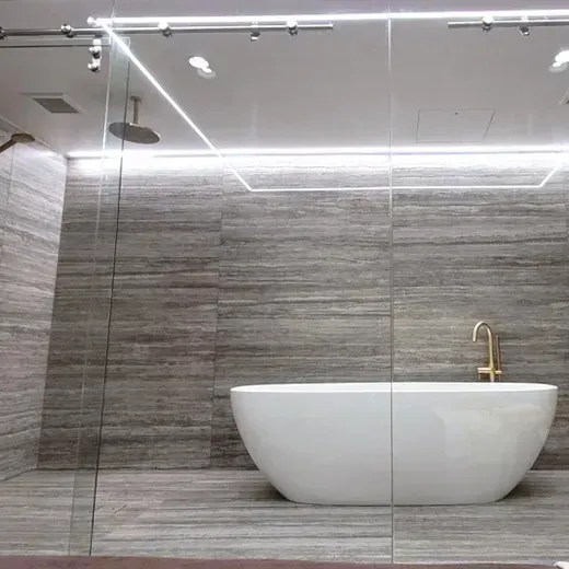 Modern bathroom with a white freestanding tub and gold faucet behind glass shower panels.