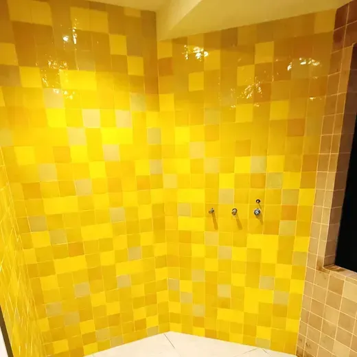 Yellow tiled shower corner with chrome fixtures and a dark doorway opening on the right