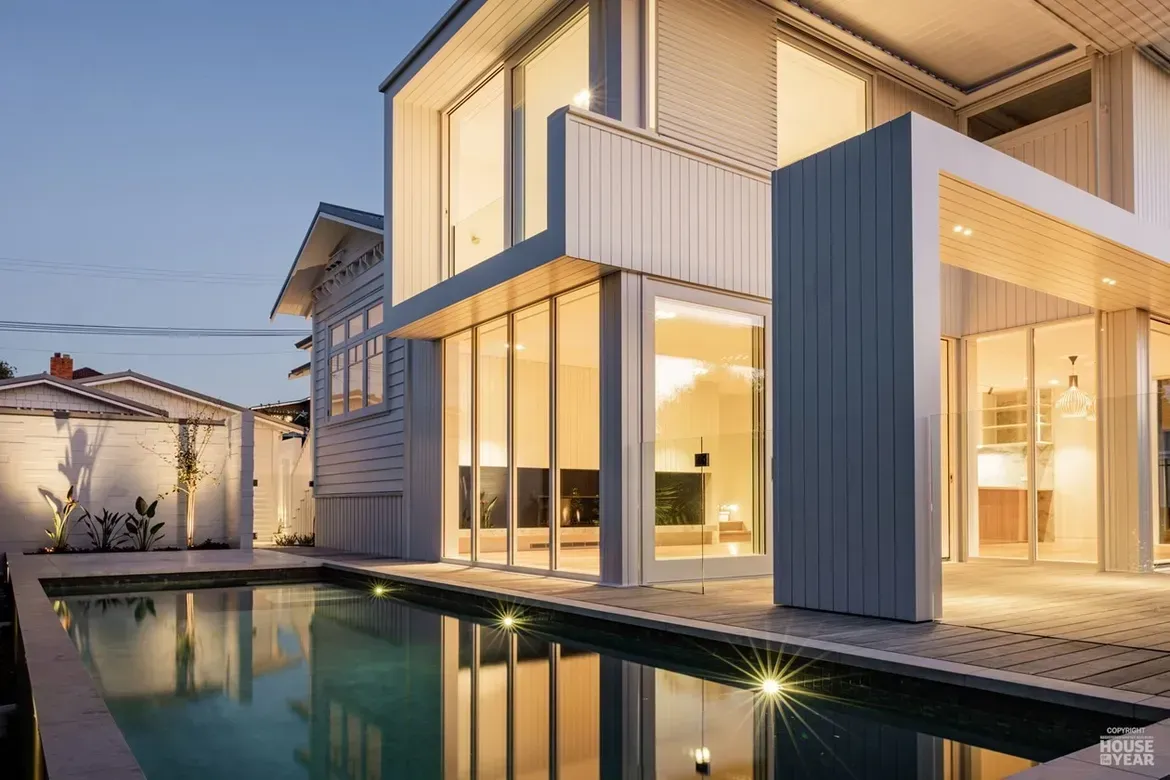 Modern two-story house with lit windows and a pool at dusk