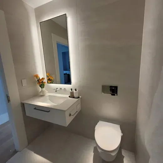 Small modern bathroom with wall-mounted sink, mirror, flowers, and toilet in neutral tones