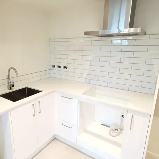 Modern white kitchen with black sink, subway tile backsplash, and stainless steel range hood