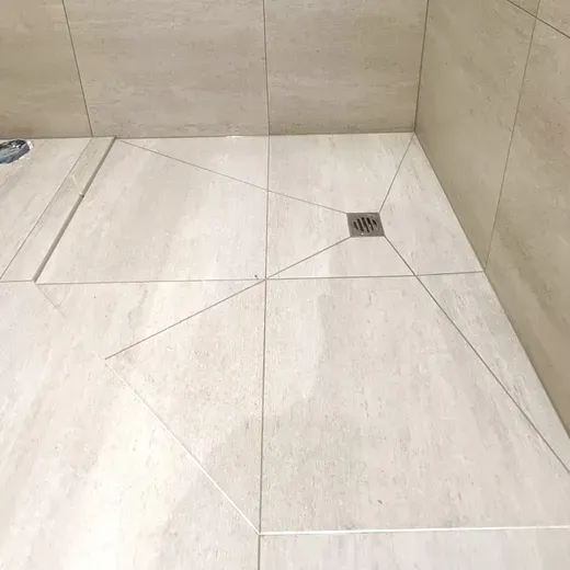 Empty beige tiled shower floor with a small square drain in the corner.
