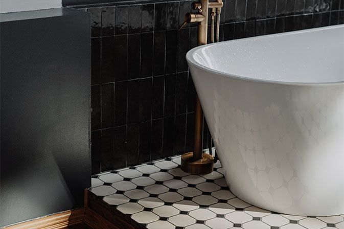 White freestanding bathtub beside black tile wall and black-and-white hexagon floor tiles
