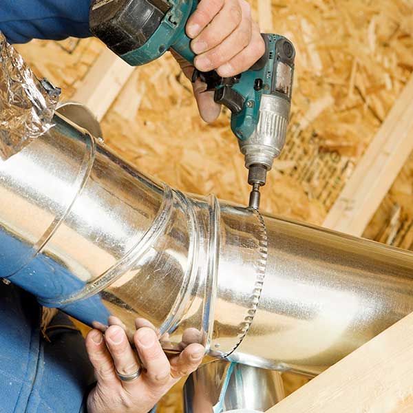 Worker using a drill to fasten shiny metal HVAC ducting in a construction setting