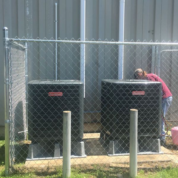 Person working beside two large black outdoor units behind a chain-link fence