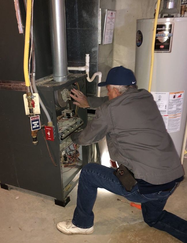 Technician kneels beside a furnace, adjusting wiring in a utility room.