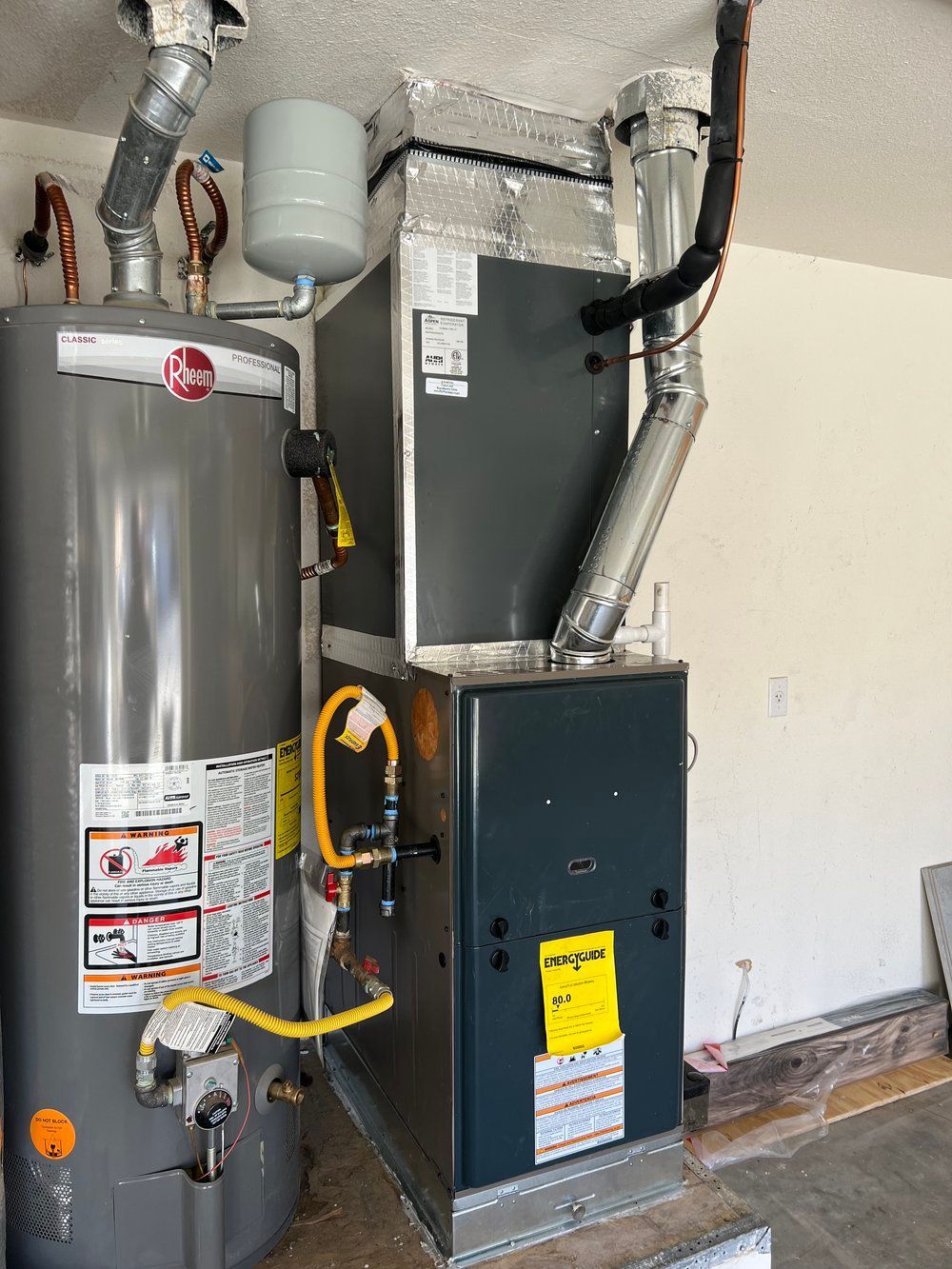 A water heater and a gas heater are sitting next to each other in a garage.