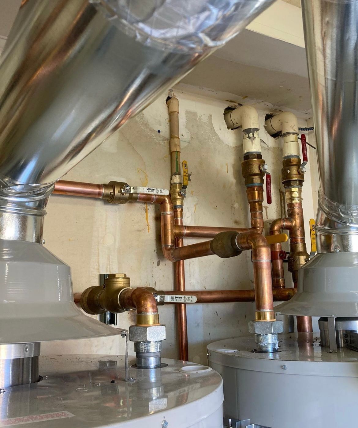 Two water heaters are sitting next to each other in a room with copper pipes.