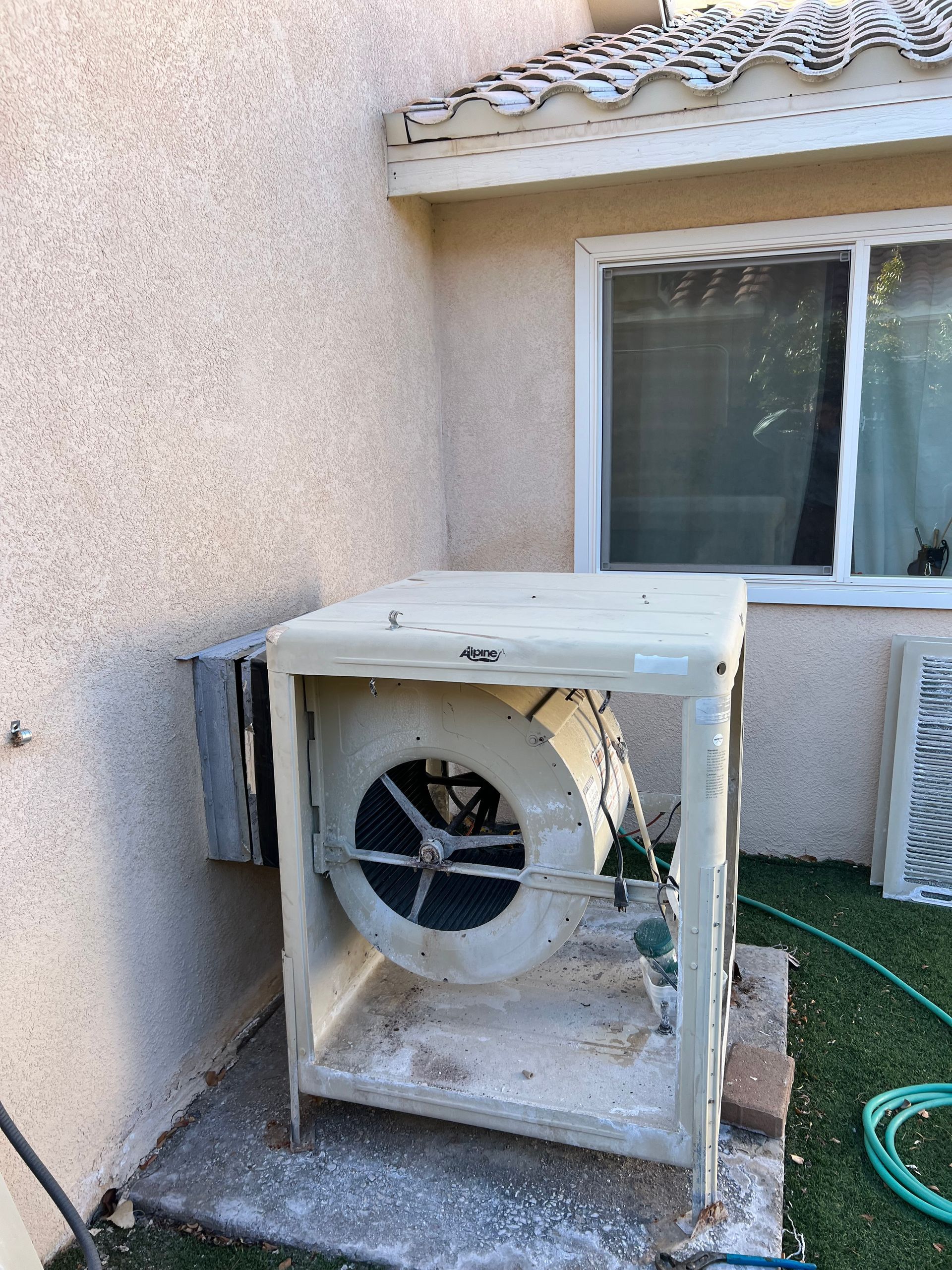 A fan is sitting outside of a house next to a window.