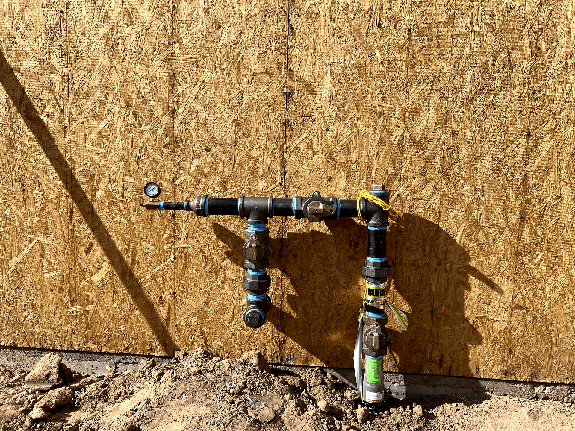 A water pipe is sitting in the dirt in front of a wooden wall.